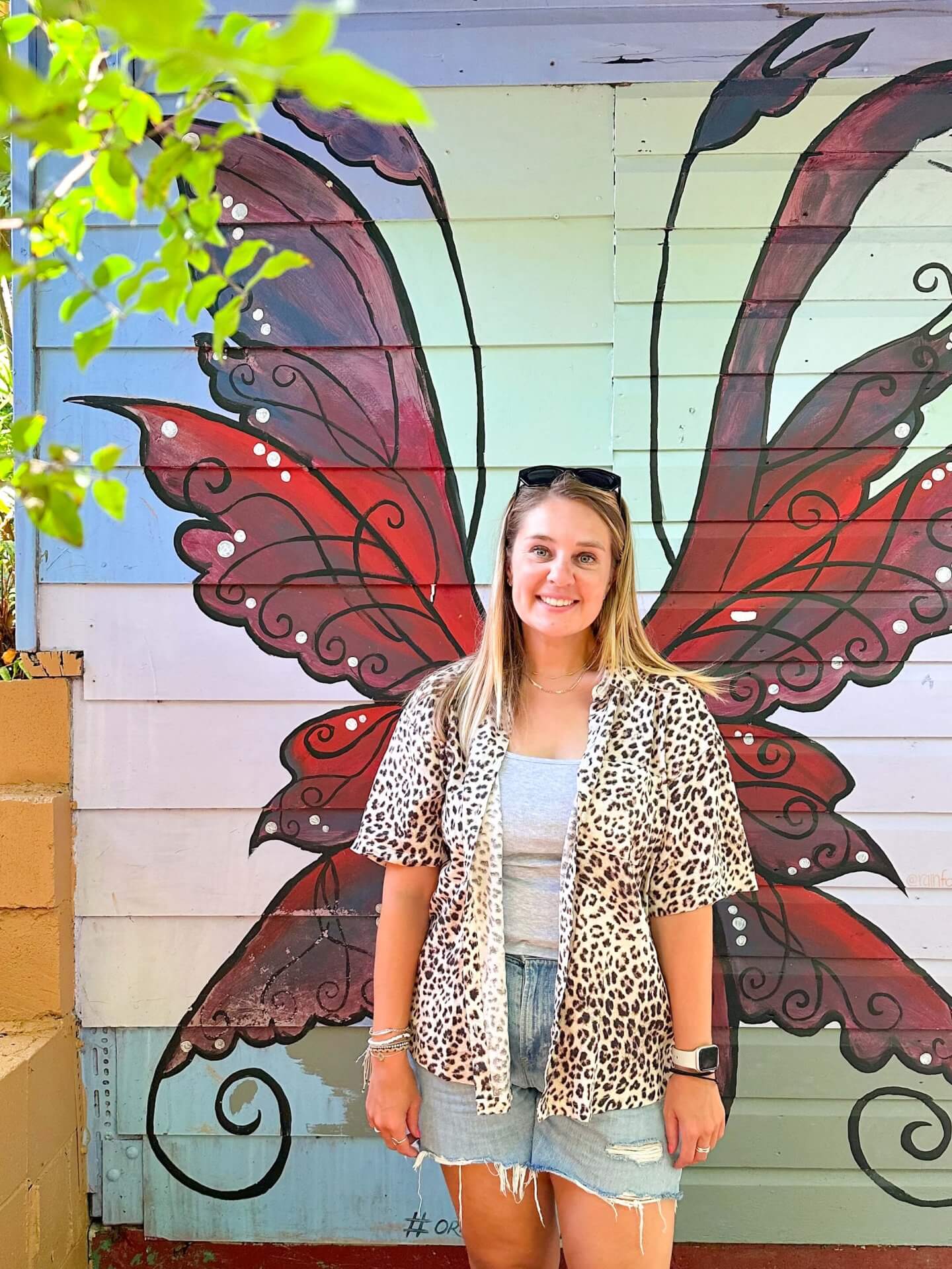 image of a woman standing in front of colourful butterfly wings painted on a wall in Kuranda Original Market