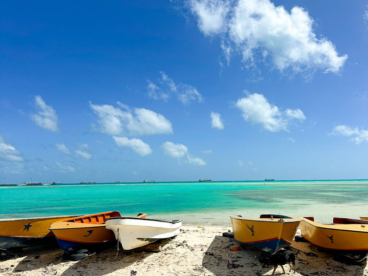 Yellow and white boats rest on a sandy beach in Betio, Kiribati, with vibrant turquoise water and a blue sky with white clouds in the background.