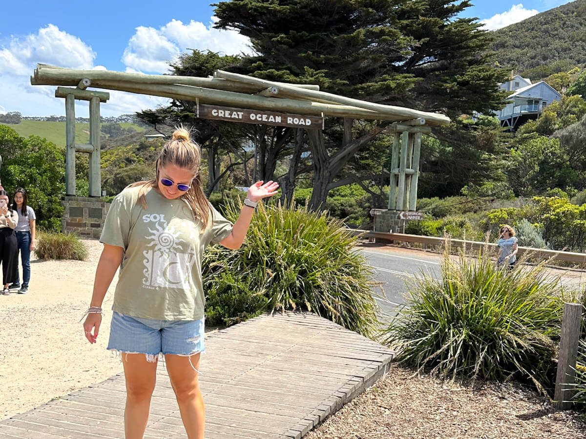 Charlie standing in front of the Memorial Arch on the Great Ocean Road. She is looking down and has her hand in the air