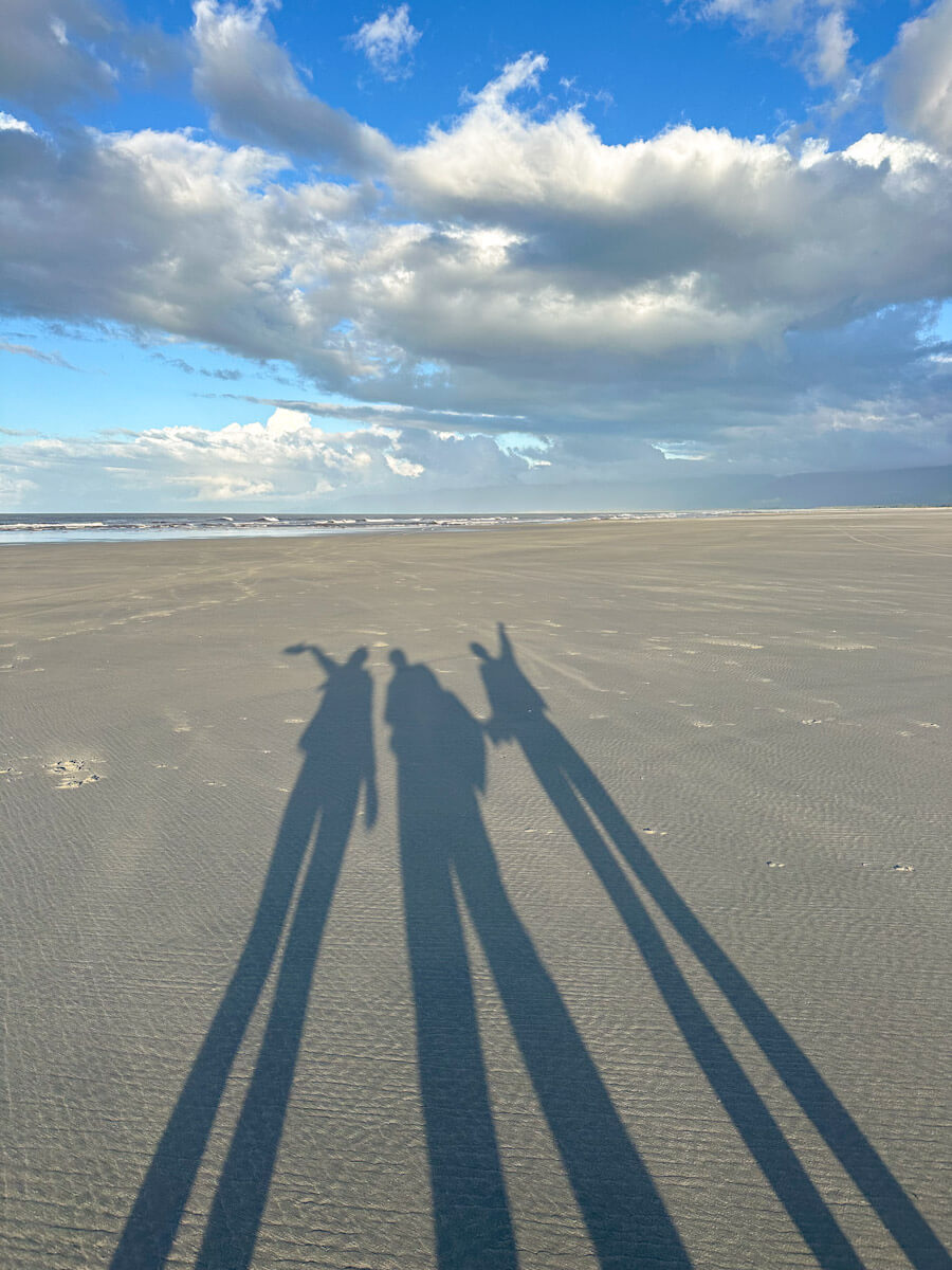 The tall shadows of three people at sunset. Their arms are outstretched