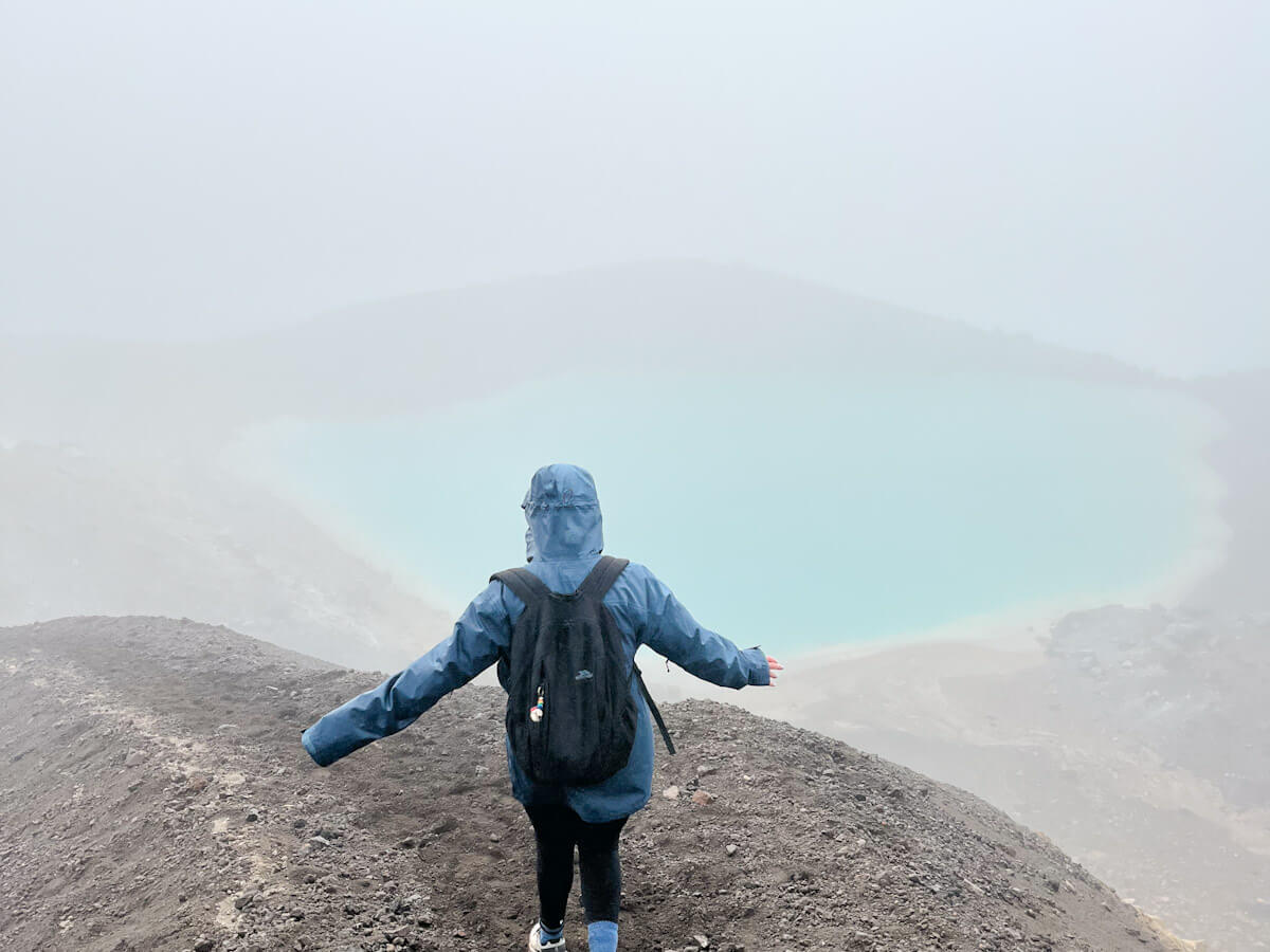 Charlie is looking out over the vibrant blue Emerald Lake on a misty day during the Tongariro Alpine Crossing in New Zealand, showcasing the unique volcanic landscape.