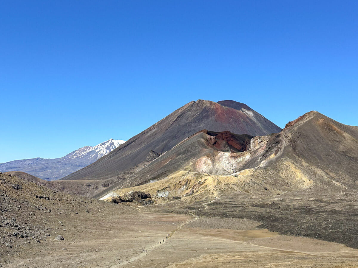 Expansive view of Mount Ngauruhoe and Red Crater, showcasing the dramatic volcanic landscape of the Tongariro Alpine Crossing with a distant snow-capped peak in New Zealand.