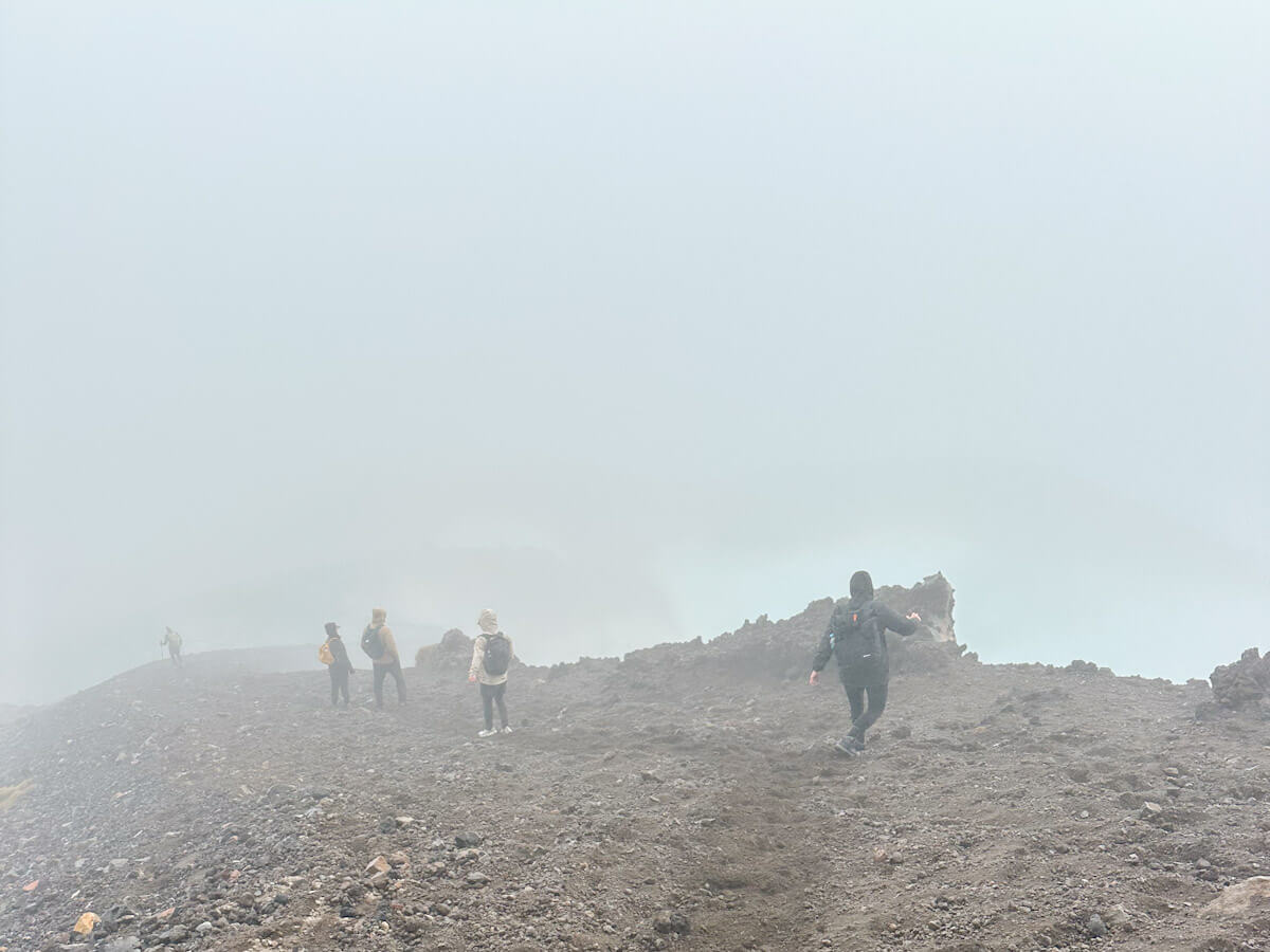 Hikers navigating a rocky, foggy section of the Tongariro Alpine Crossing trail, with limited visibility creating an atmospheric hiking experience in New Zealand.