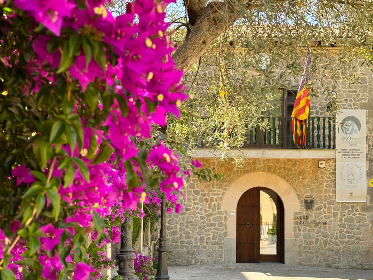 The town hall of Valldemossa, Spain, framed by vibrant pink bougainvillea flowers in the Jardins Rei Joan Carles