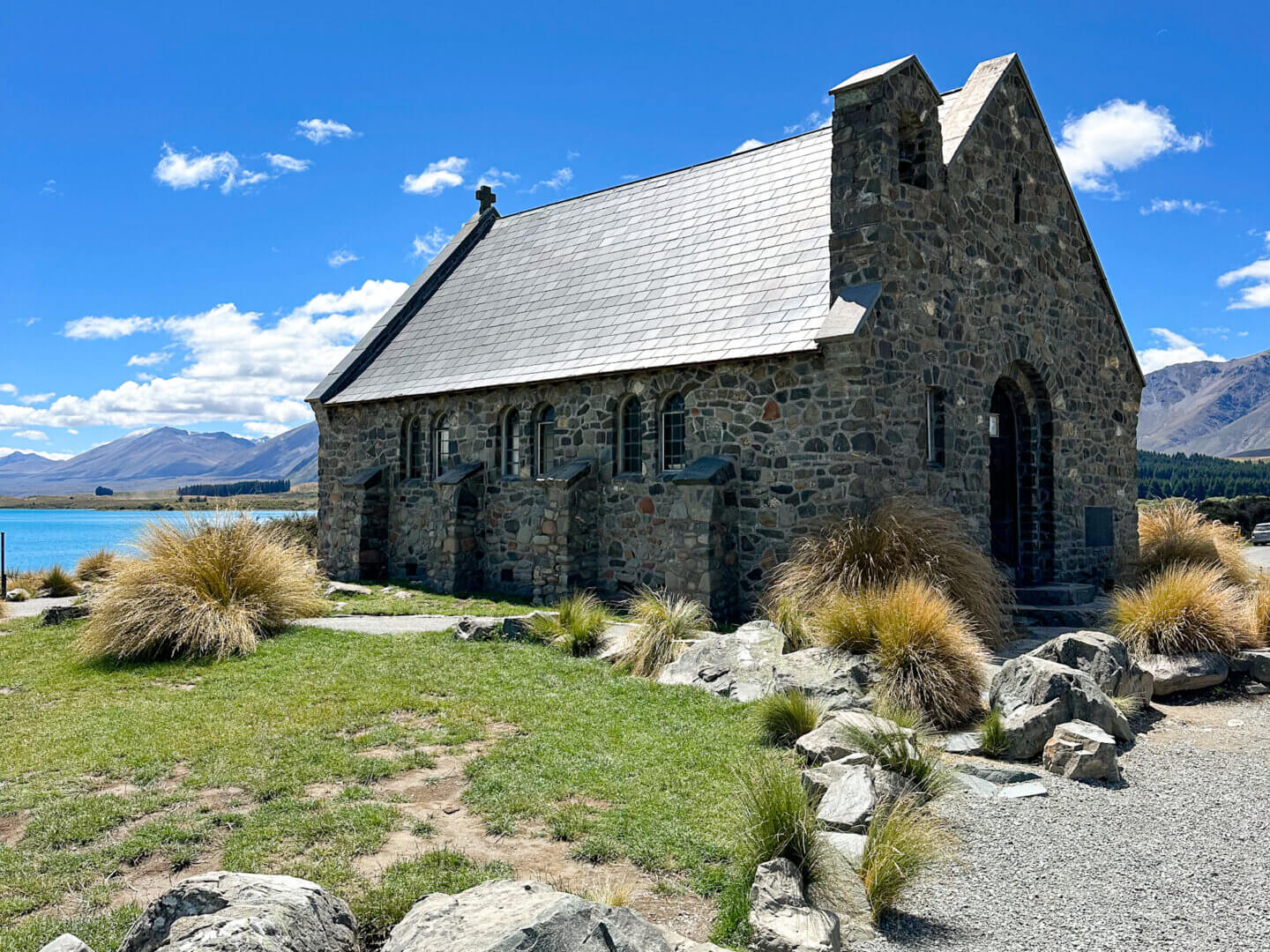 A small stone church, the Church of the Good Shepherd, sits on the shore of the turquoise Lake Tekapo with the Southern Alps visible in the background, a popular sightseeing spot on New Zealand's South Island.