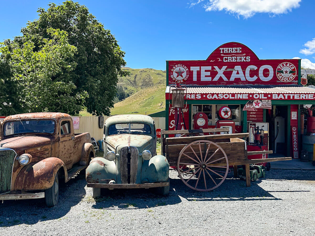 A vibrant red Three Creeks Texaco retro gas station with vintage cars and rustic decor, a quirky roadside attraction and museum in the South Island of New Zealand.