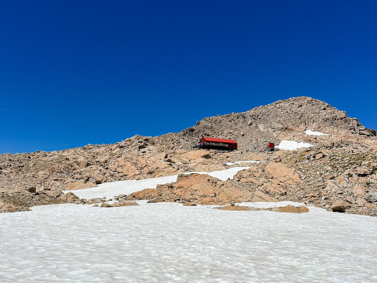 The bright red Mueller Hut stands on a rocky, snow-dusted ridge, a key landmark for hikers on the trail to Mueller Hut in Aoraki/Mount Cook National Park.