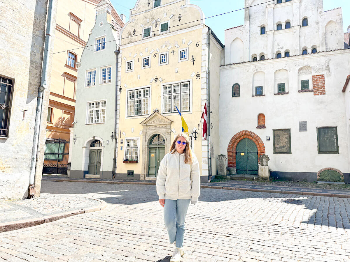What to do in Riga: A woman standing on the cobblestone street in front of the famous Three Brothers Houses (Trīs brāļi), the oldest residential complex in Riga.