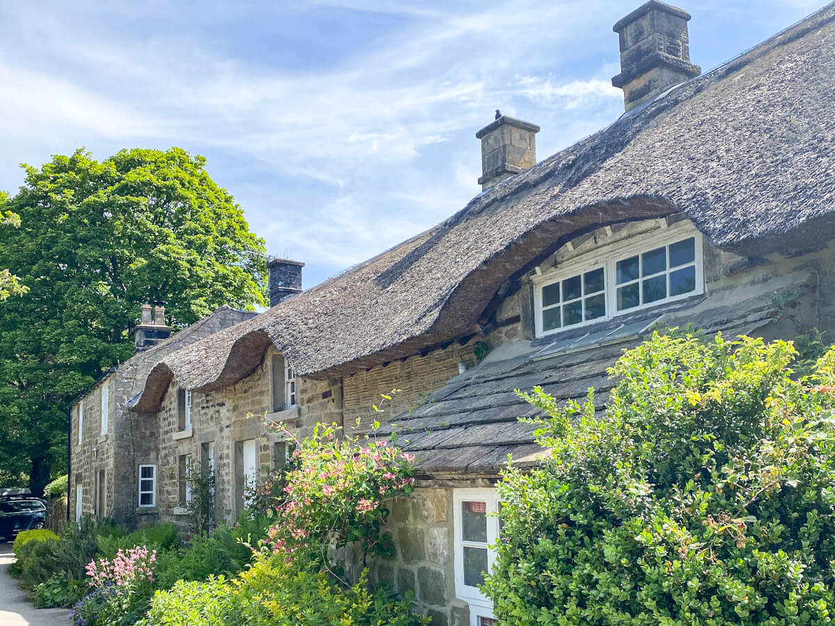 Beautiful thatched-roof stone cottages in Baslow, one of the best villages in the Peak District, surrounded by colorful flower gardens and bright green shrubbery.