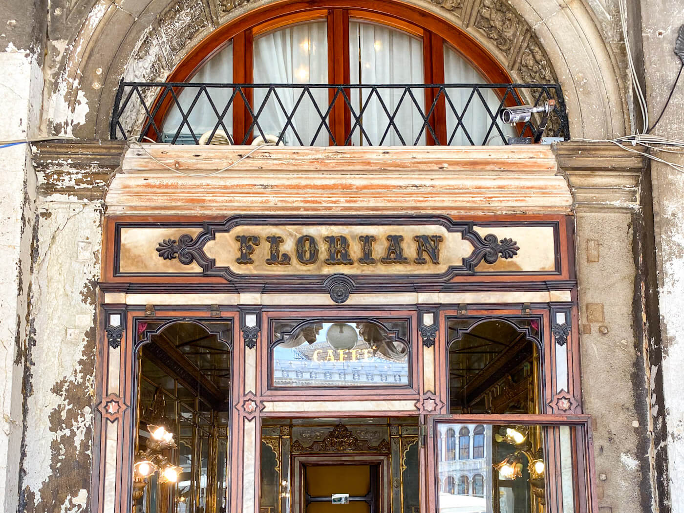 The historic carved wood and glass storefront of Caffรจ Florian, showing the warm glow of interior lamps inviting visitors inside.