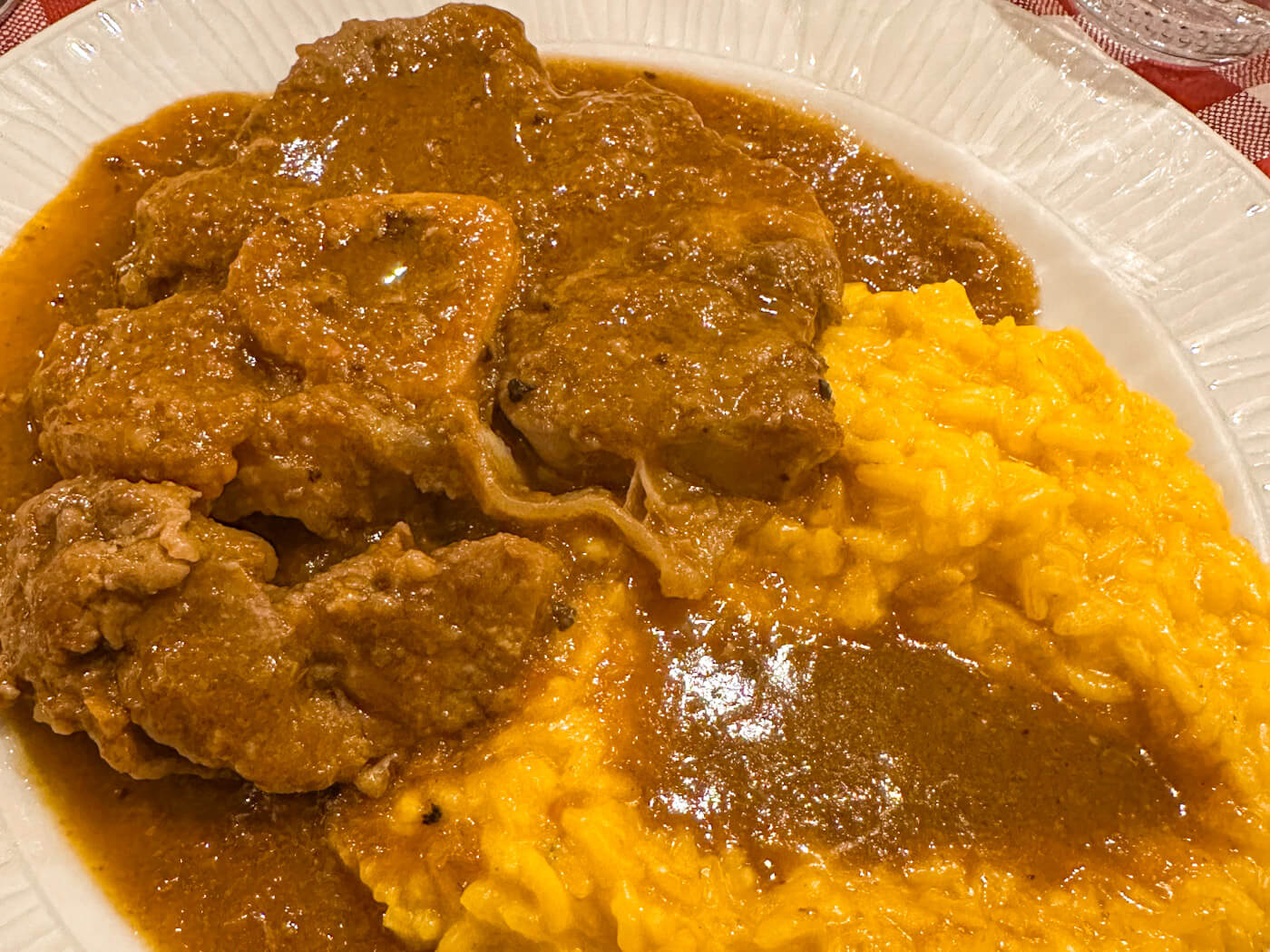 A close-up, top-down shot of a traditional Milanese dish featuring a tender, braised Ossobuco (veal shank) served with a rich brown gravy alongside a vibrant yellow Risotto alla Milanese on a white textured plate.
