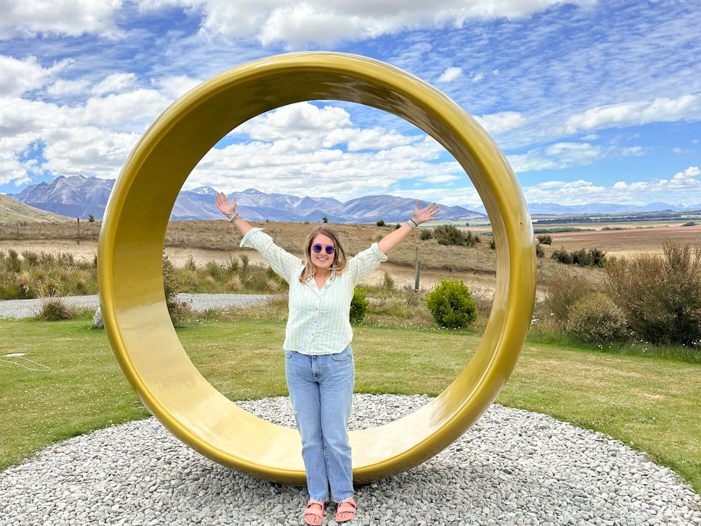Charlie stands with her arms outstretched inside the giant golden One Ring sculpture near Twizel, New Zealand. While not a film set itself, it is located near the Pelennor Fields, one of the famous Lord of the Rings Filming Locations