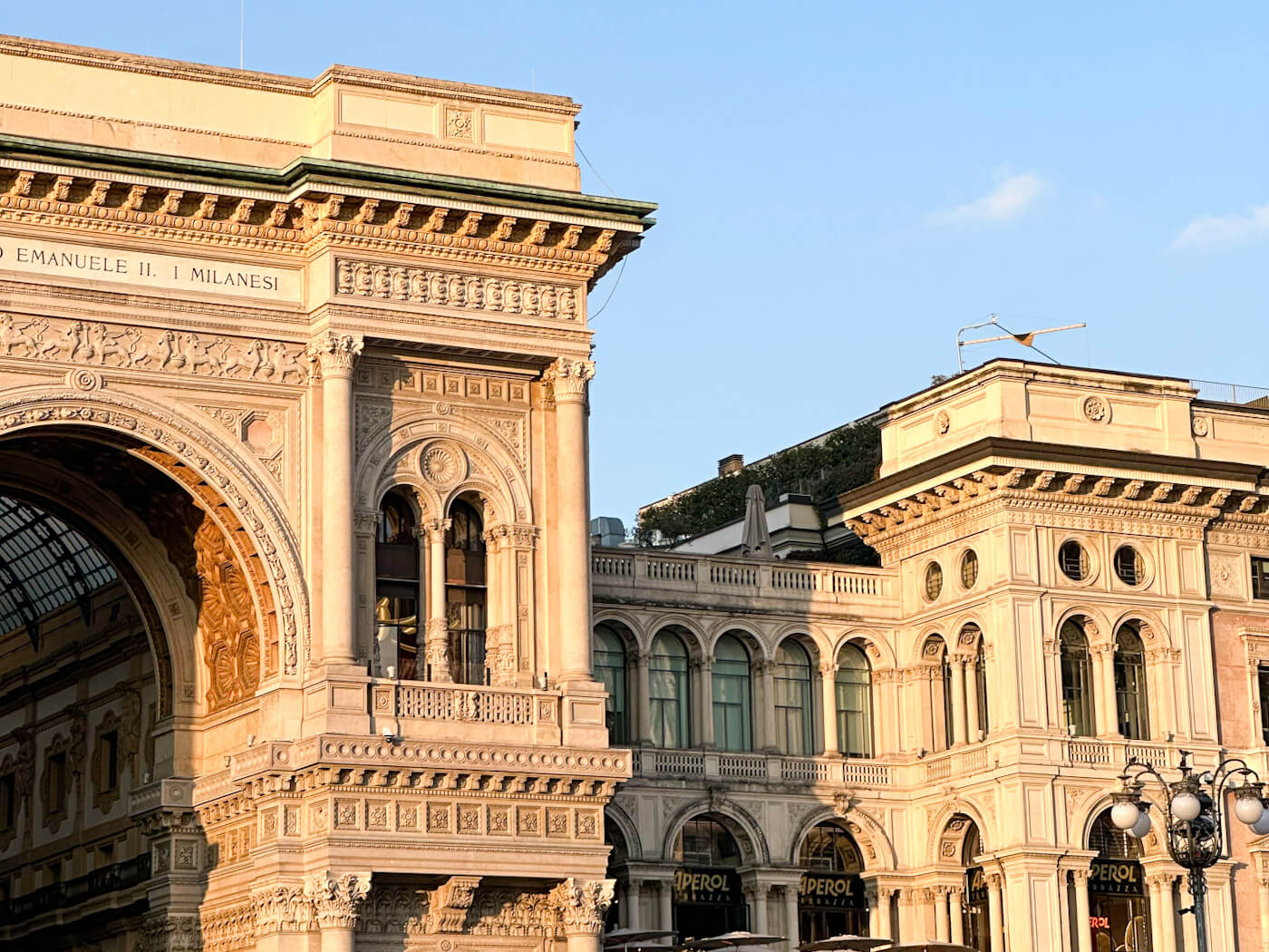 A close-up architectural detail of the neoclassical buildings flanking the Piazza del Duomo, captured in the warm, golden light of late afternoon, highlighting the ornate balconies, arched windows, and Corinthian columns.