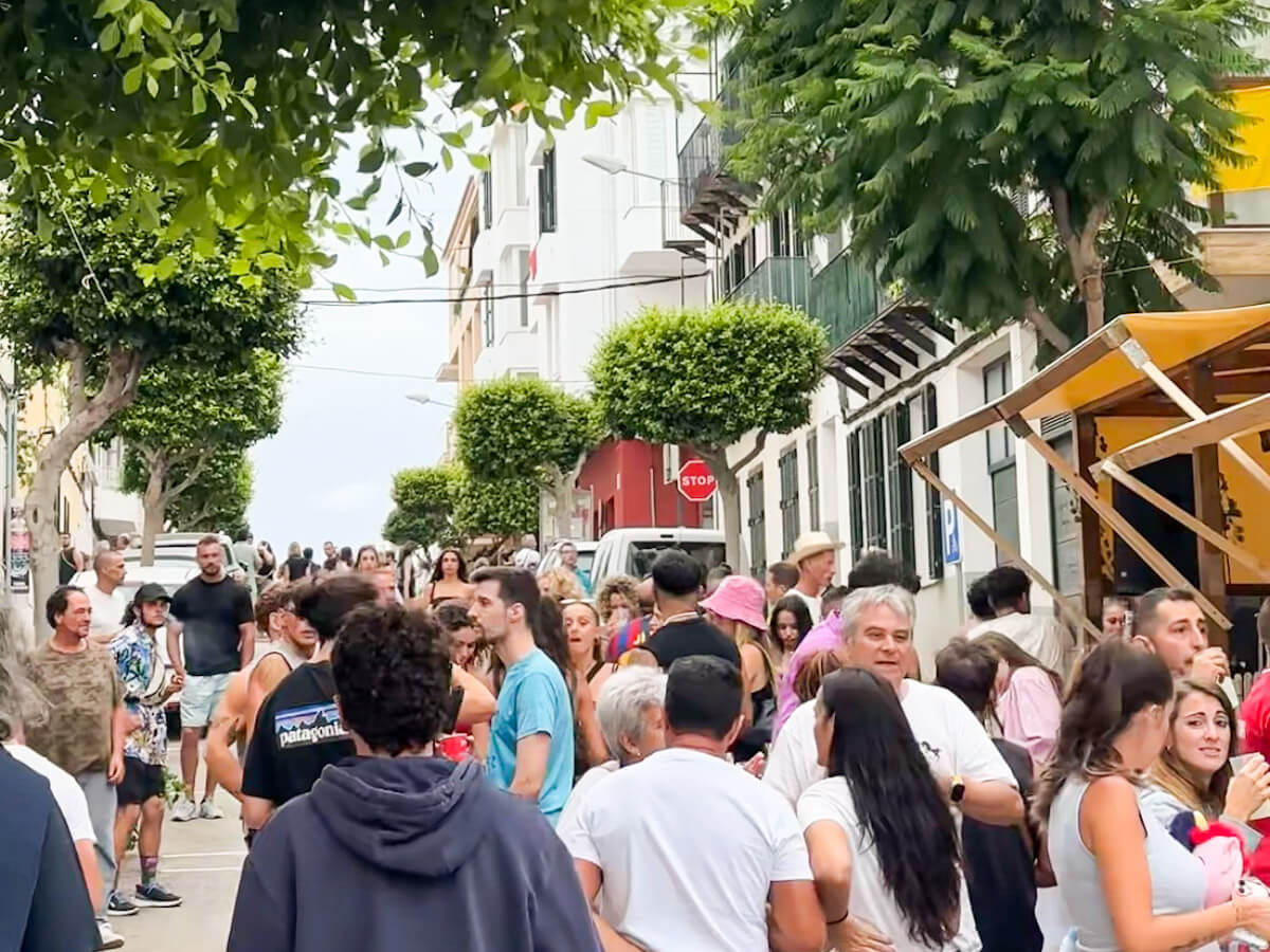 Large crowds of locals and visitors filling the streets of Es Castell during the Sant Jaume Menorca fiesta, with street bars and food stalls set up along the roadside