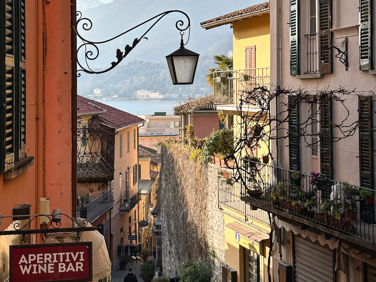 Looking down the cobbled steps of Salita Serbelloni in Bellagio, with colourful Italian buildings, iron balconies and a glimpse of Lake Como at the end of the street — a must-see stop on a day trip to Lake Como