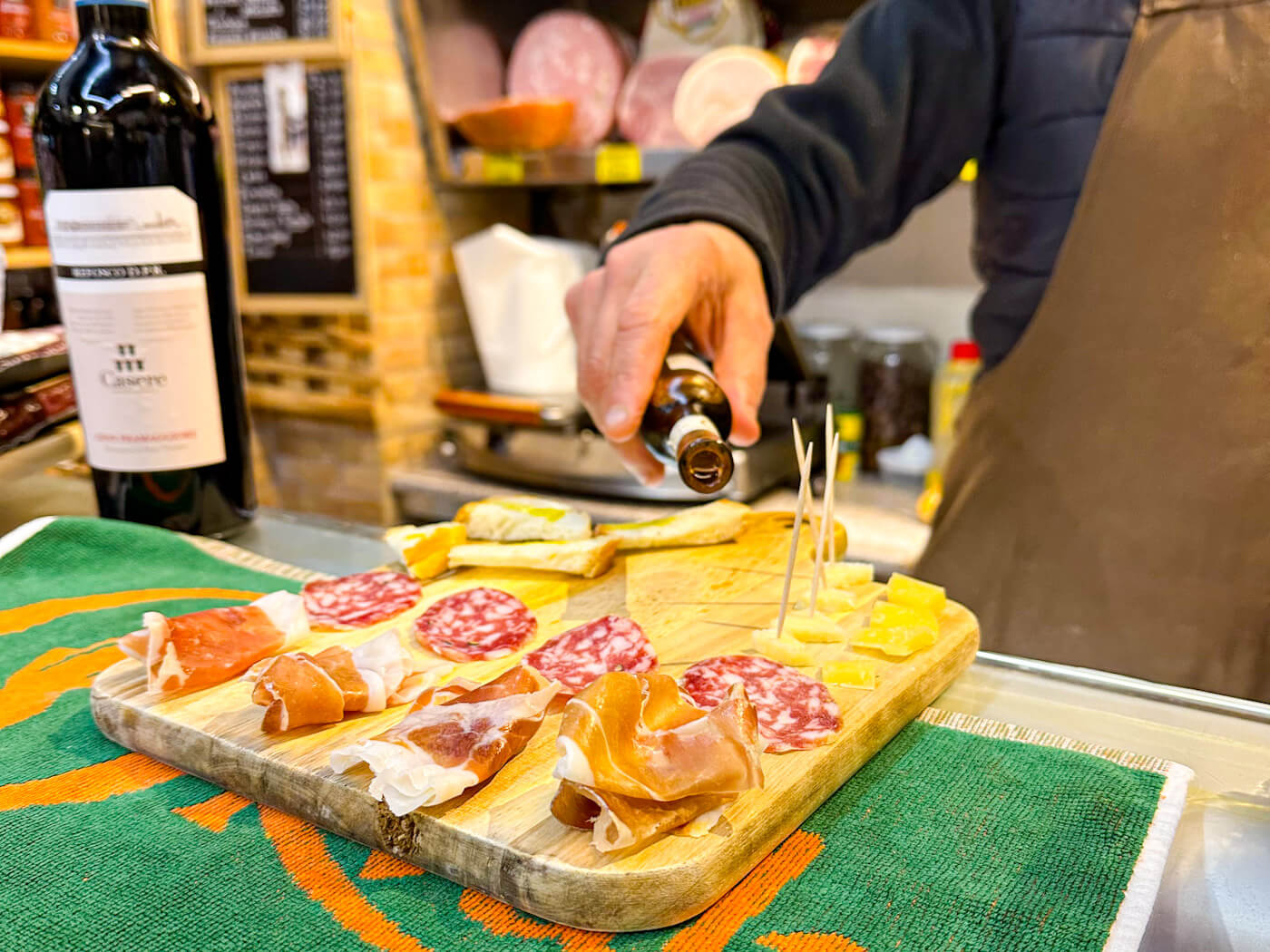 A wooden board of cured meats, cheese and bread being drizzled with truffle oil at Salumeria Roby and Giusy — a hidden gem and one of the best places for where to eat in Venice.
