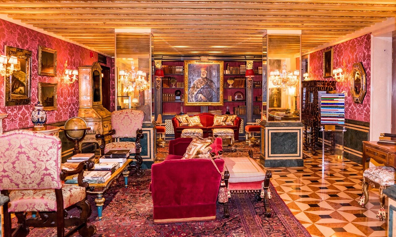 The opulent, red-damask-walled library of the Gritti Palace featuring gold-leaf ceilings, plush velvet sofas, and antique books, representing one of the most luxurious and best things to do in Venice.