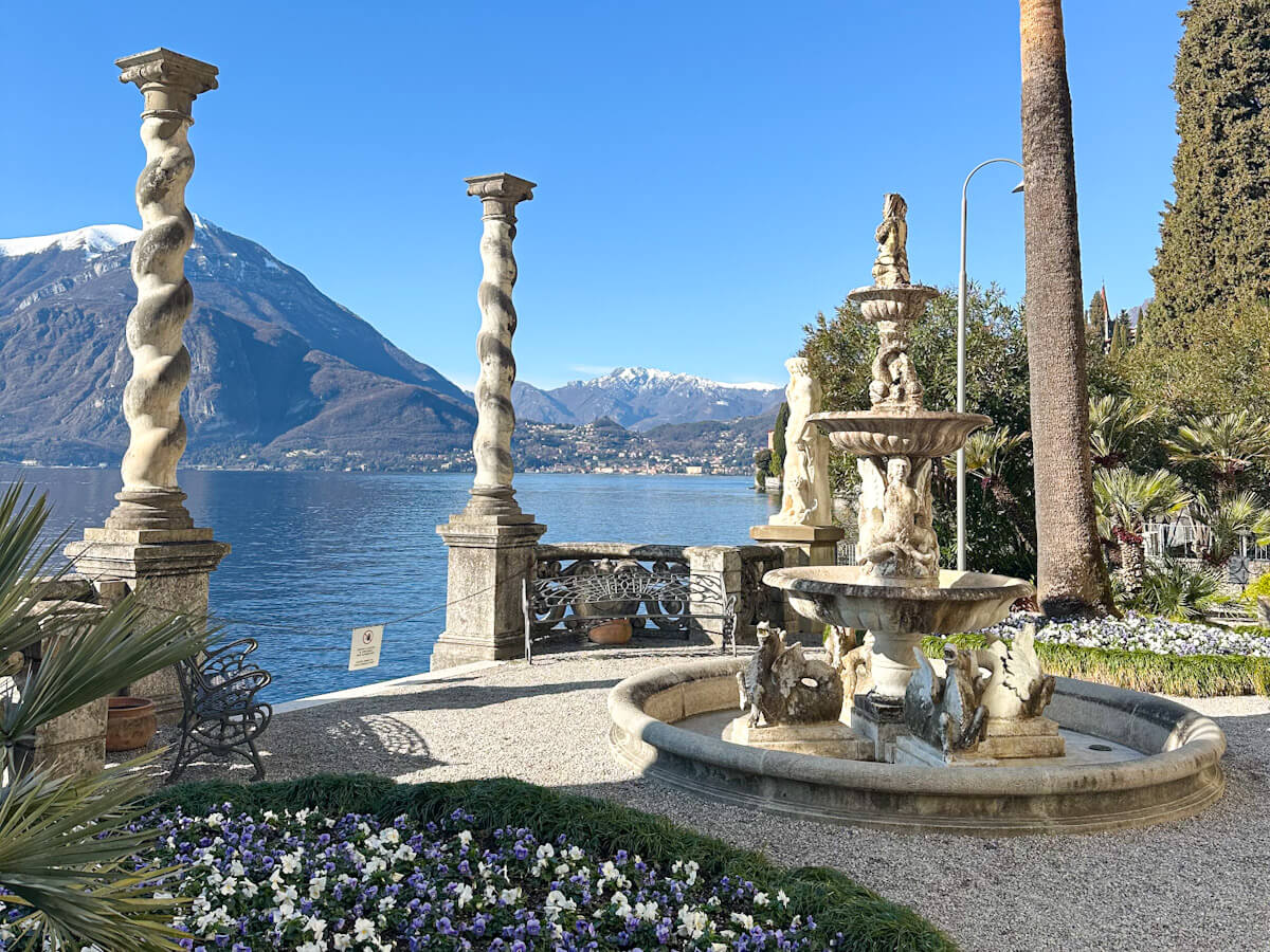 Gardens of Villa Monastero in Varenna — one of the highlights of a day trip to Lake Como, featuring ornate stone fountains, twisted columns and stunning views across the water to snow-capped mountains
