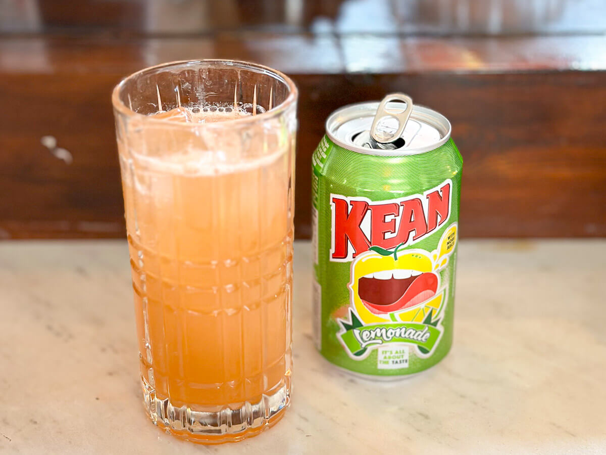 A tall crystal glass filled with a refreshing Cypriot Brandy Sour cocktail sitting on a marble bar next to a green can of KEAN lemonade, capturing a taste of what to do in Larnaca.