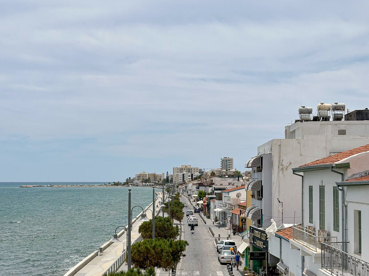 An elevated view looking down the coastal road and pedestrian walkway of Finikoudes Promenade next to the blue Mediterranean sea, showing a popular area for what to do in Larnaca.