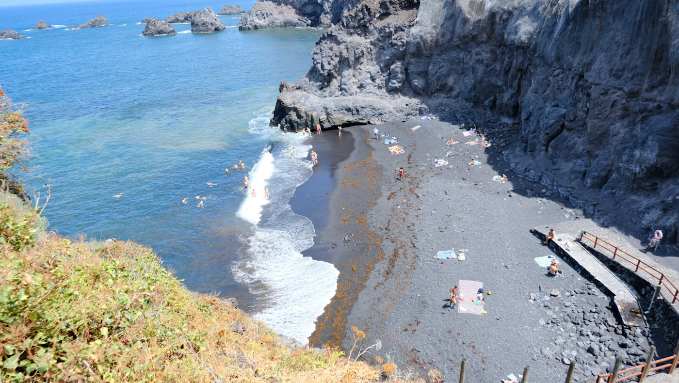 People enjoying the secluded black volcanic sand and clear blue waters of Playa de Zamora near Fuencaliente, nestled between rugged cliffs as part of things to do in La Palma.