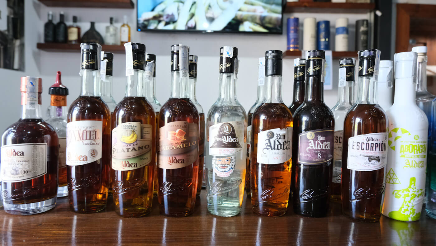 A lineup of various bottles of locally produced Ron Aldea rum and artisanal liqueurs on a wooden bar, showcasing traditional Canarian spirits as part of food and drink things to do in La Palma.