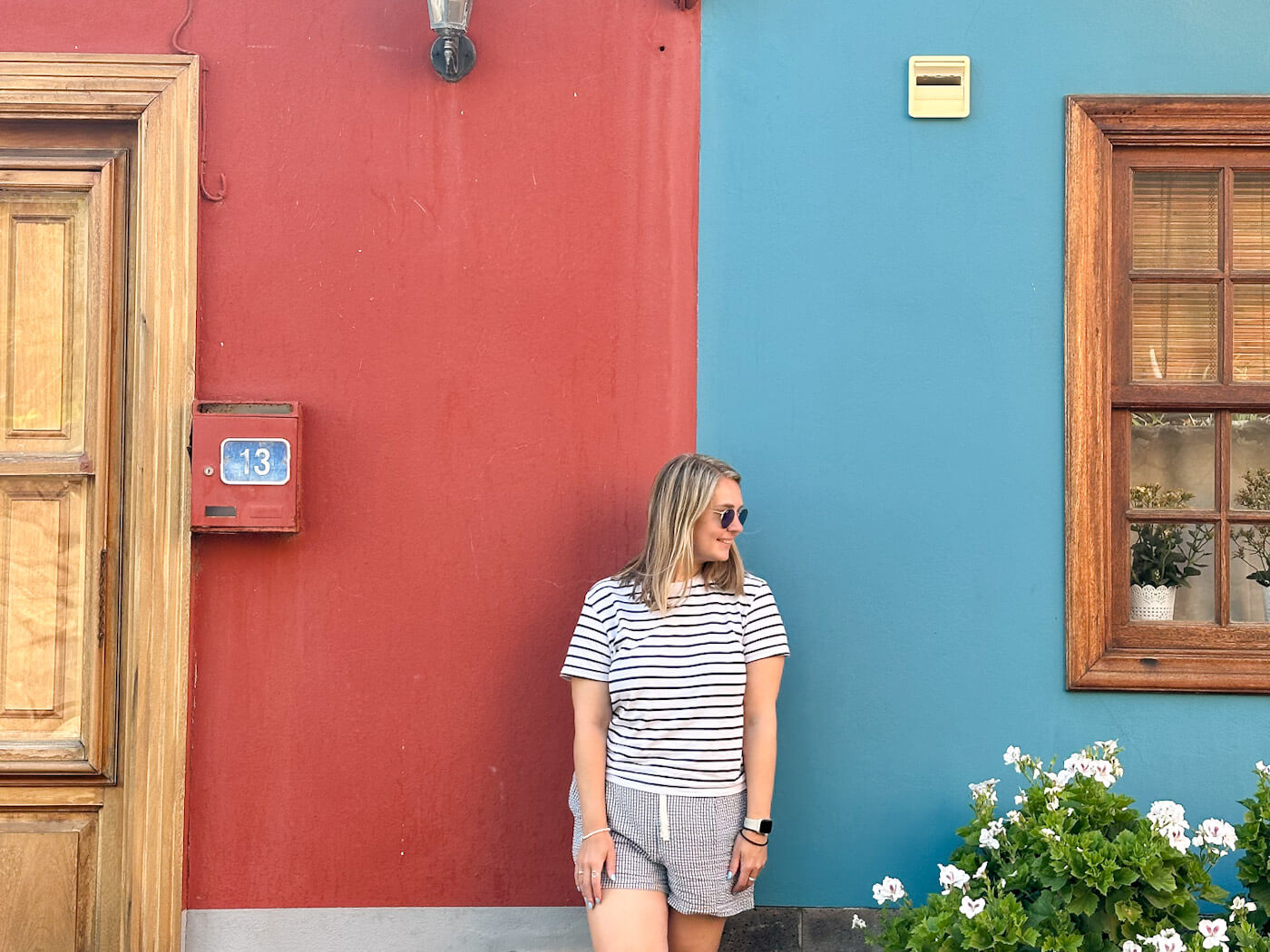 Charlie is in a striped top and shorts standing against a bright red and turquoise wall in San Andrés, highlighting colourful Canarian architecture as one of the best things to do in La Palma.
