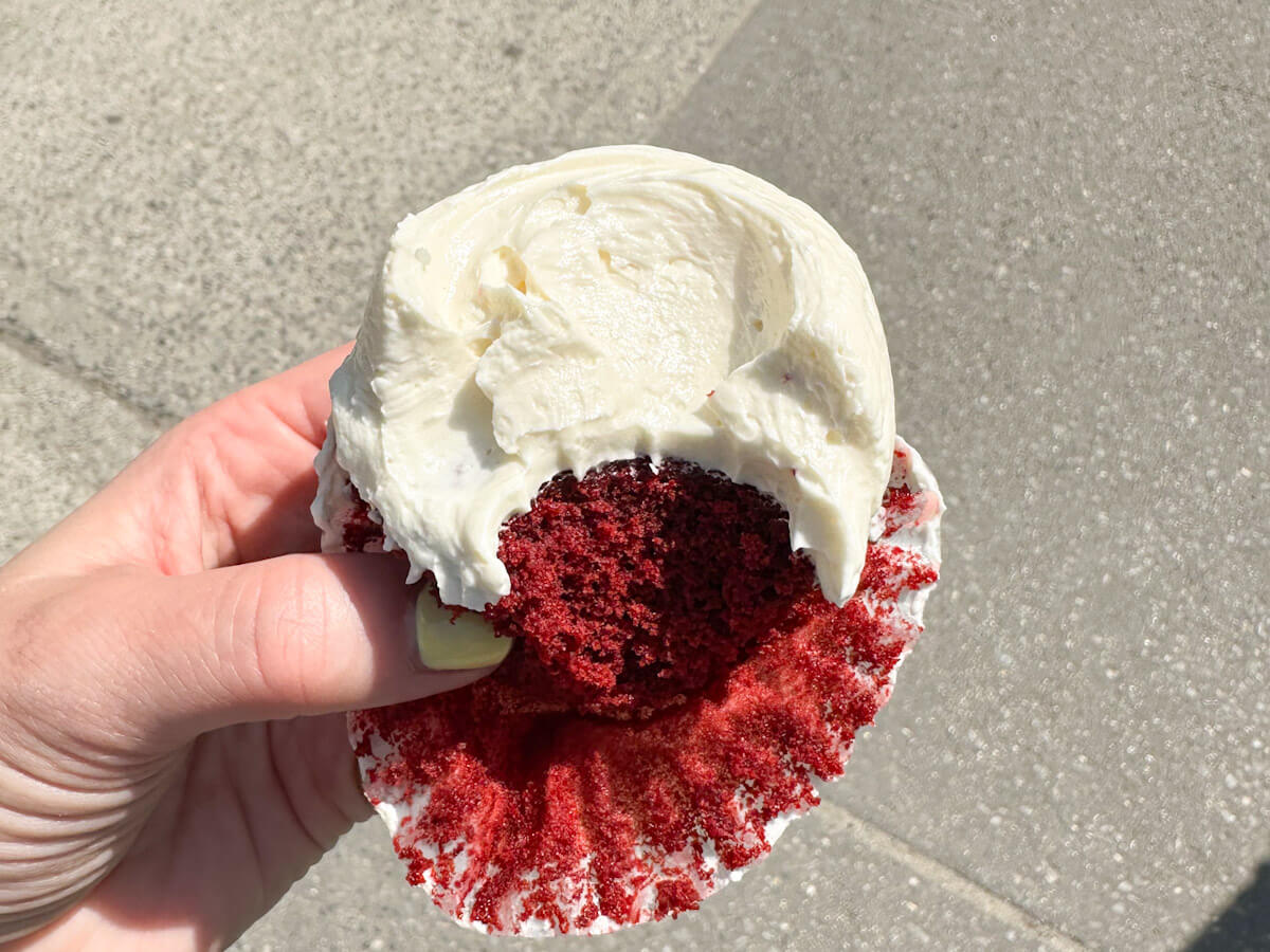 A person holding a red velvet cupcake from Magnolia Bakery in the West Village with a bite taken out, showing the rich red crumb and thick white cream cheese frosting, making it an essential sweet treat to try for food in new york.