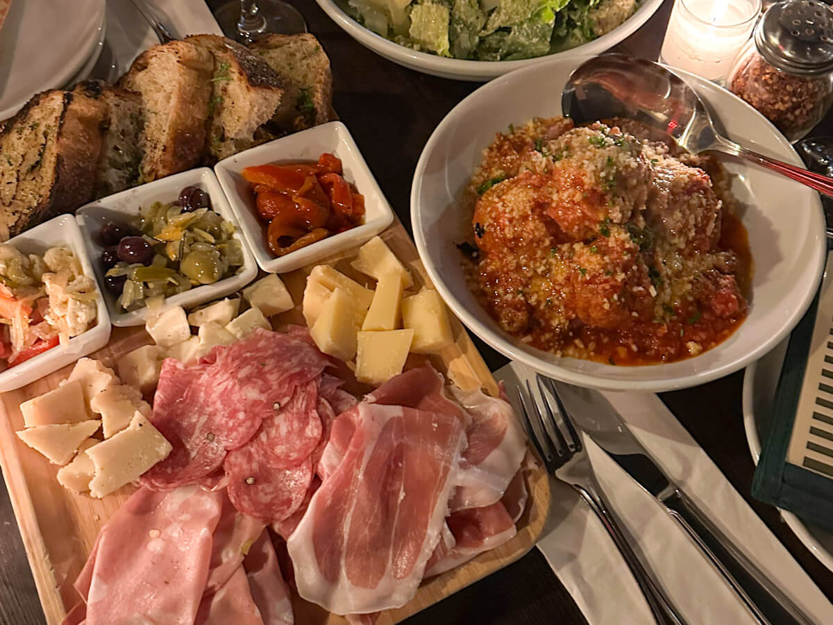 A spread of Italian food at Rubirosa featuring a charcuterie board with cured meats, cheeses, olives, and sliced bread alongside a large bowl of meatballs in tomato sauce, highlighting the classic dining options for food in new york.