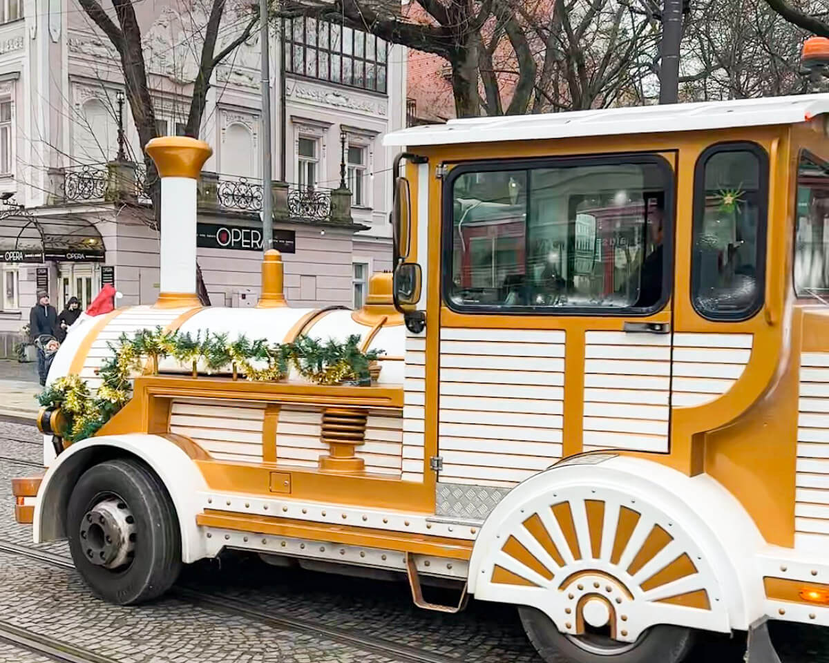 The festive tourist road train decorated with garlands for the Christmas season in Bratislava, Slovakia, running along the cobblestone streets past historic buildings.