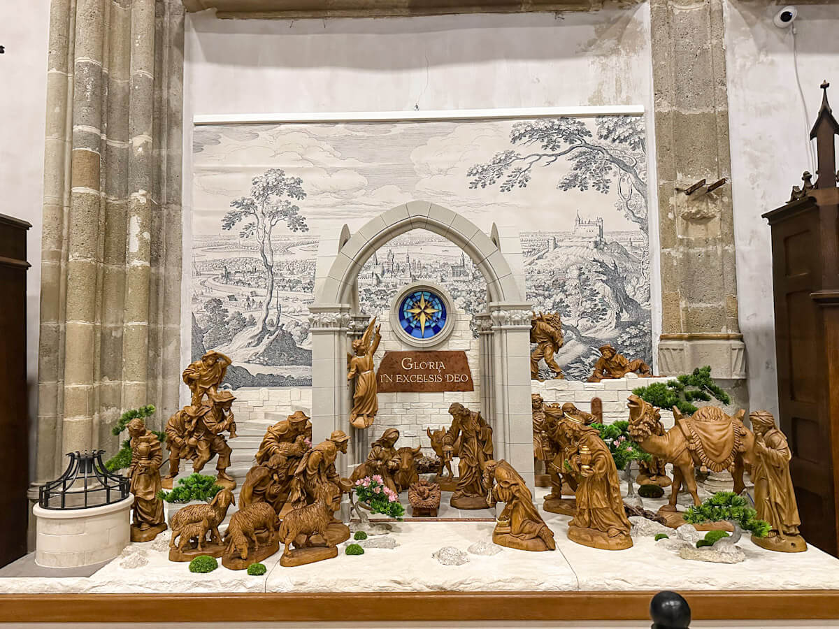 Intricate wooden nativity scene displayed inside St. Martin's Cathedral during the Bratislava Christmas Market, featuring carved figures, camels, and an arched backdrop with a "Gloria in Excelsis Deo" sign.