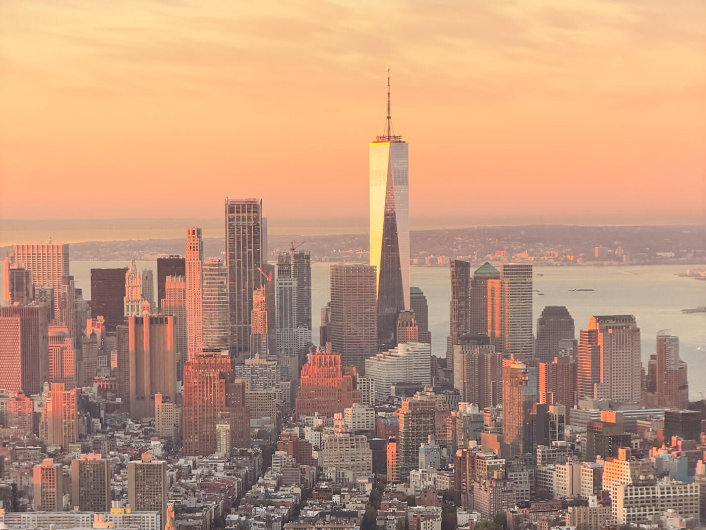 Panoramic aerial view of the Lower Manhattan skyline and One World Trade Center glowing in golden morning sunlight during a visit to New York in fall. As seen from the Empire State Building at sunrise.