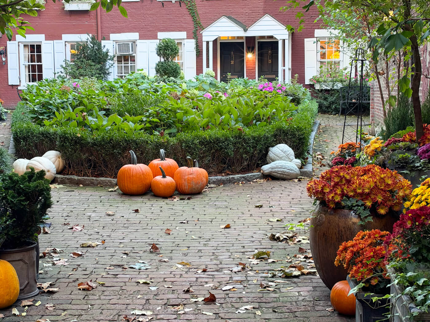 Charming brick courtyard of Grove Court decorated with orange and white pumpkins, gourds, and colorful potted autumn flowers.