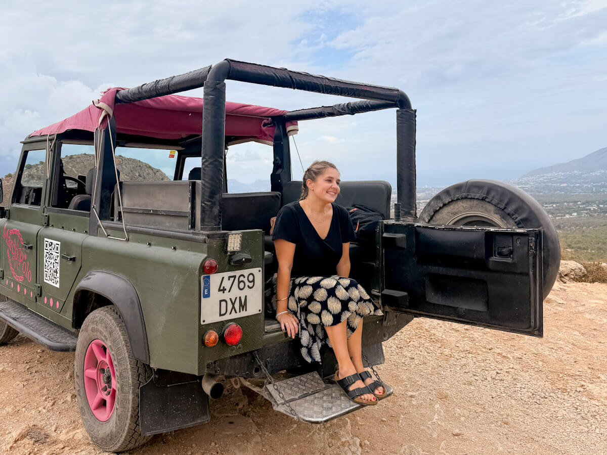 Charlie is smiling while sitting on the open back tailgate of a green Jeep Safari vehicle overlooking the mountains, showing exciting outdoor activities and what to do in Benidorm without partying.