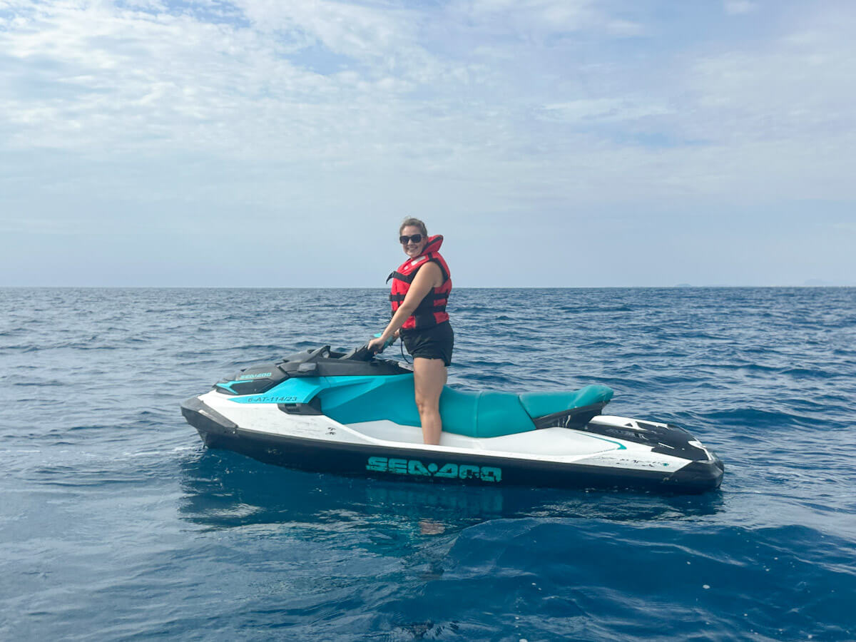 Woman wearing a red life jacket smiling on a teal and white Sea-Doo jet ski in the middle of the Mediterranean Sea, highlighting thrilling water sports and what to do in Benidorm without partying.