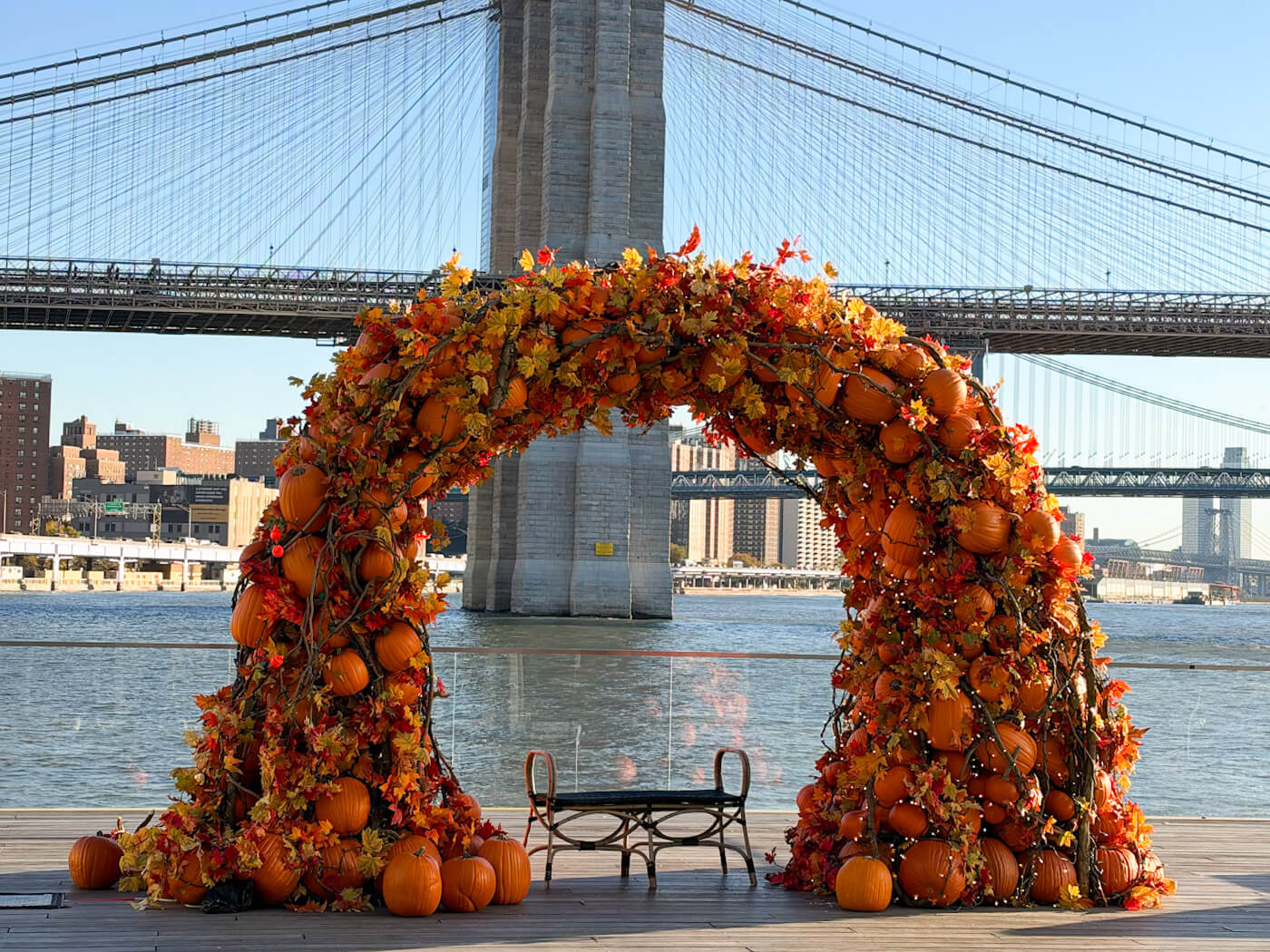 A large decorative pumpkin arch with autumn leaves frame on pier 17 overlooking the Brooklyn Bridge in New York in fall.