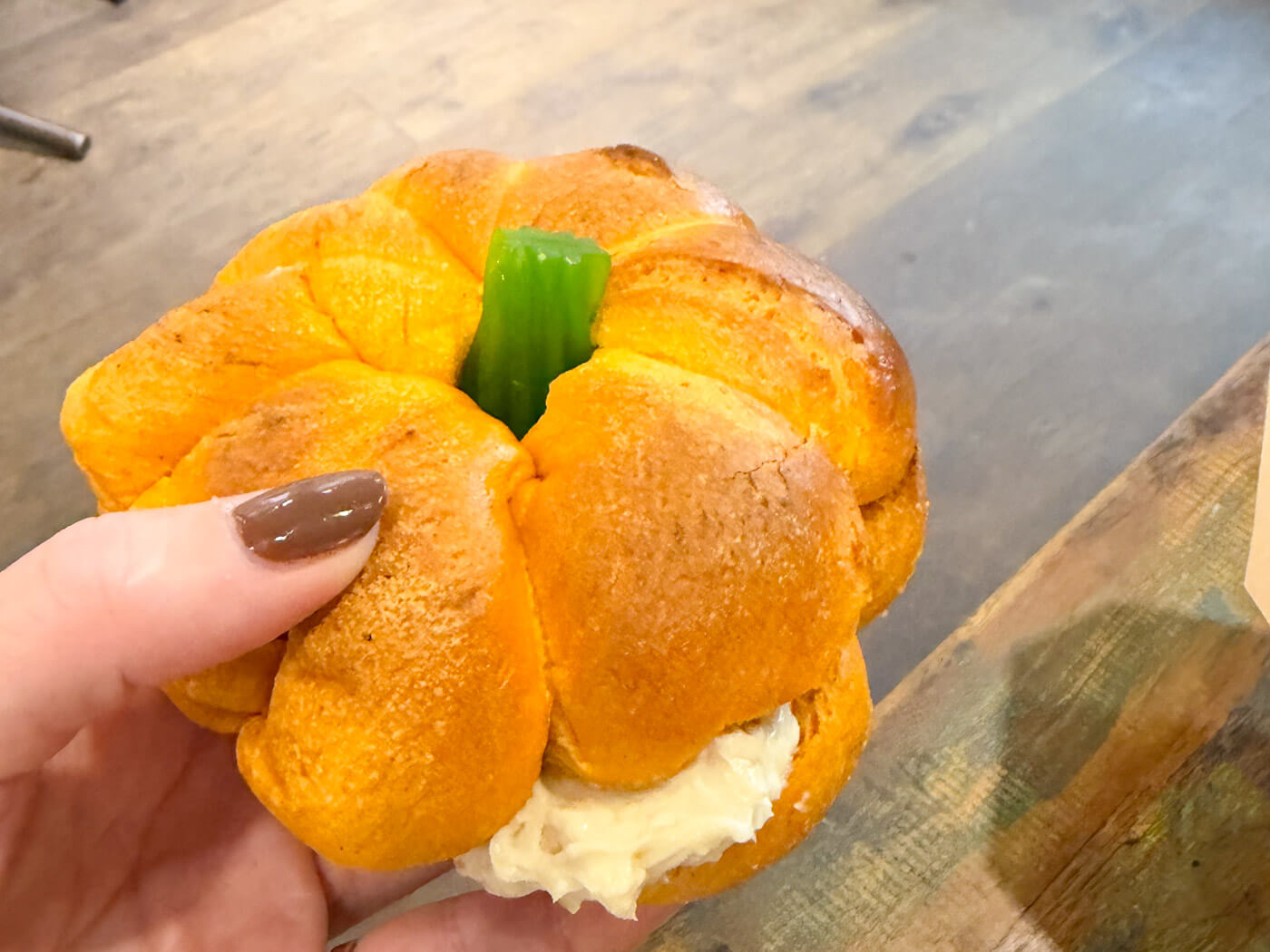A hand holding a festive pumpkin-shaped bagel stuffed with cream cheese spread from Scoop in New York