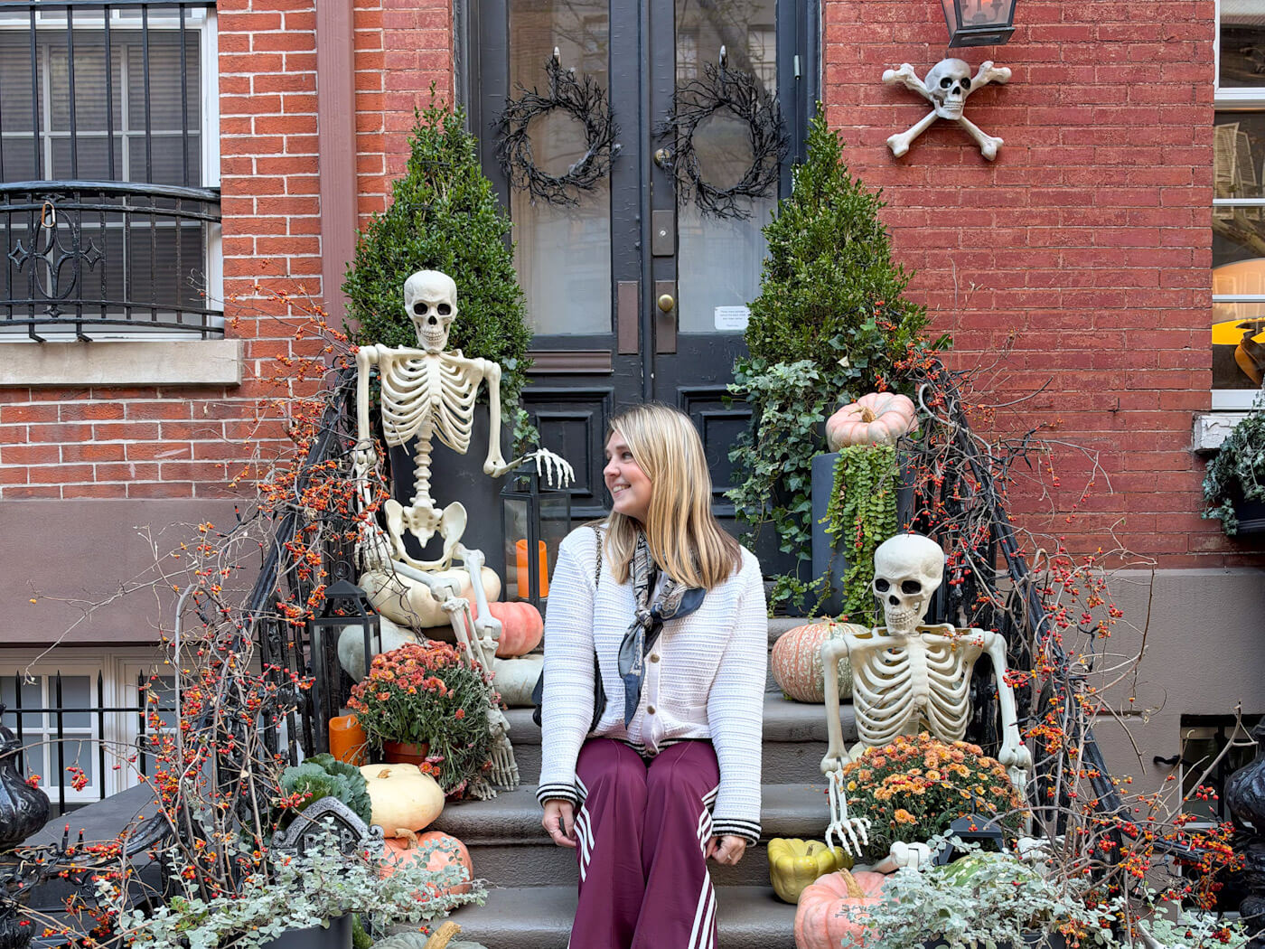 Charlie sitting on the steps of a brownstone stoop decorated with skeletons, pumpkins, and autumn plants for Halloween in New York in fall.