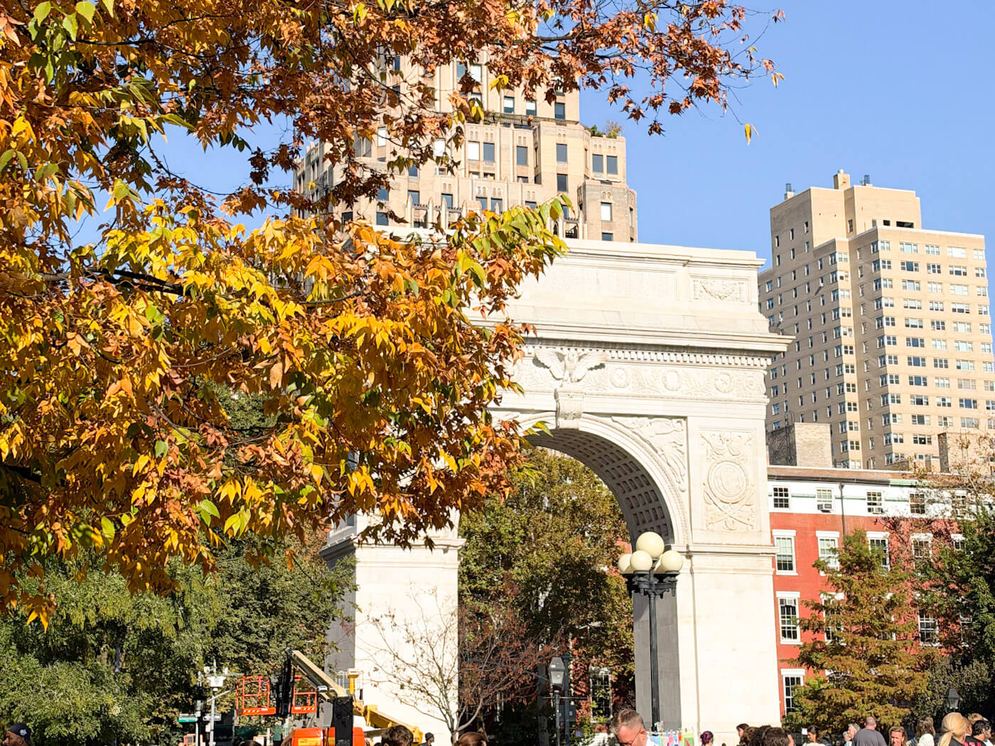 Washington Square Arch framed by golden yellow and brown fall leaves on a sunny day.